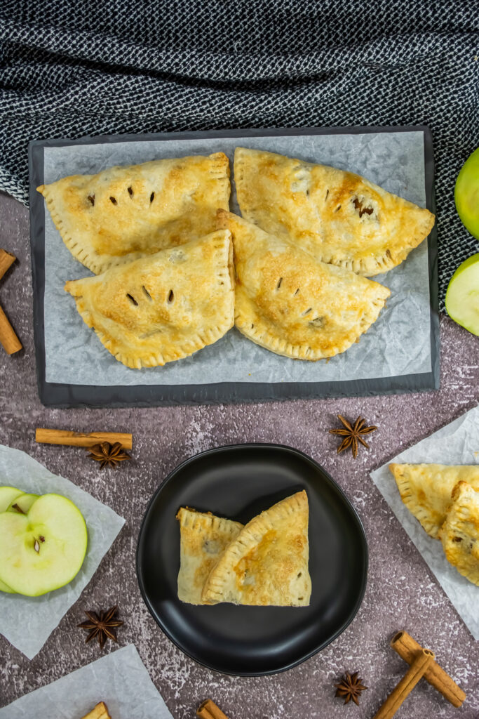 baked apple empanadas (pies) on tray with cinnamon sticks around