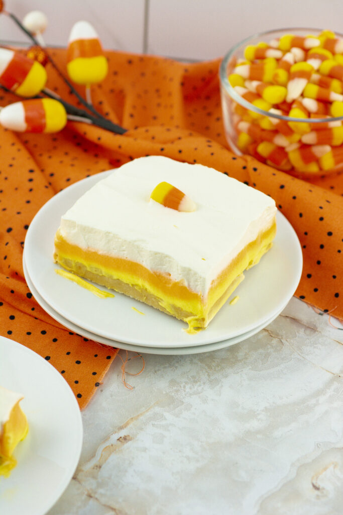 no bake candy corn lush on white plates in front of candy corn in glass bowl