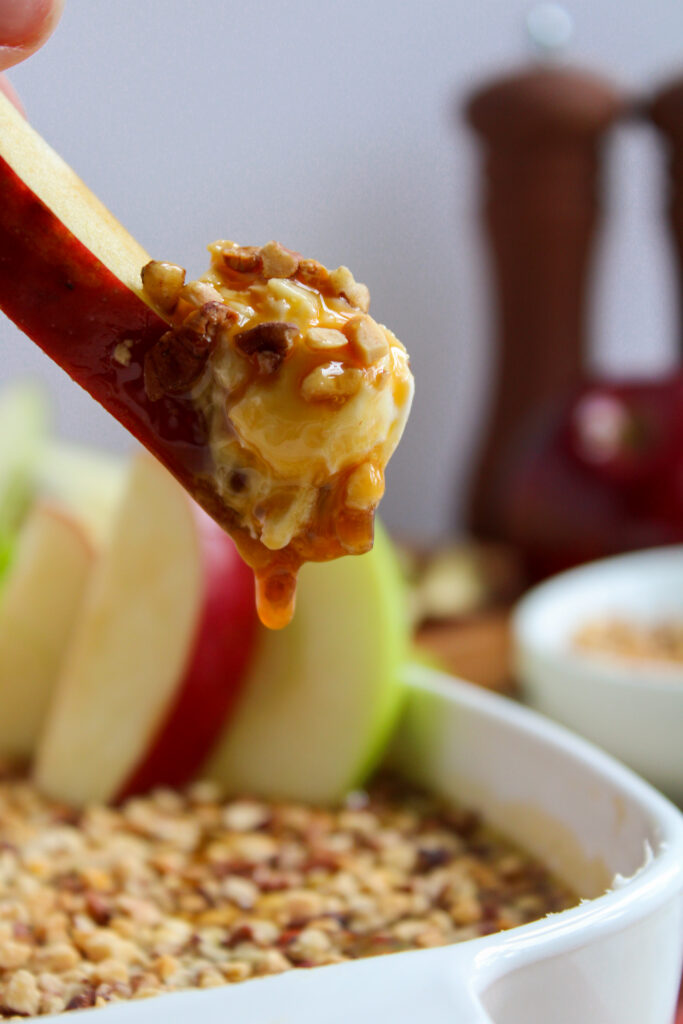 apple slice with cream cheese caramel apple dip on top of serving bowl