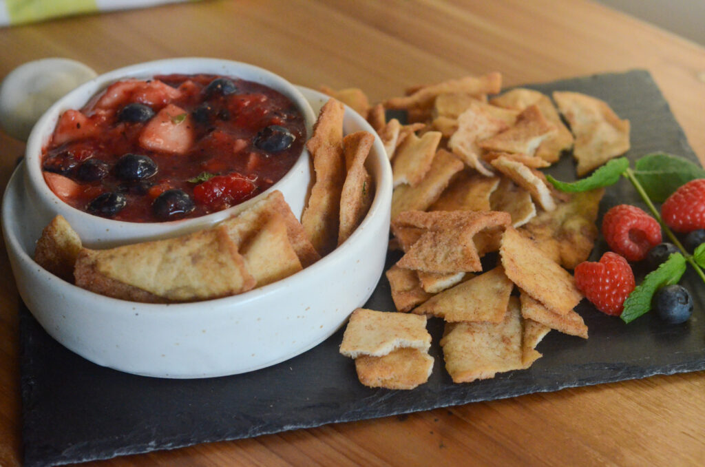 berry fruit salsa in white bowl on black slate tray with cinnamon sugar chips and fruit