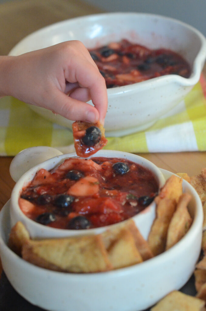 person dips cinnamon sugar pita chip into berry fruit salsa