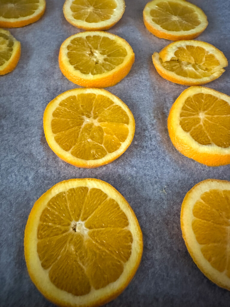 sliced oranges on parchment paper for dried citrus wheels for Christmas gifts