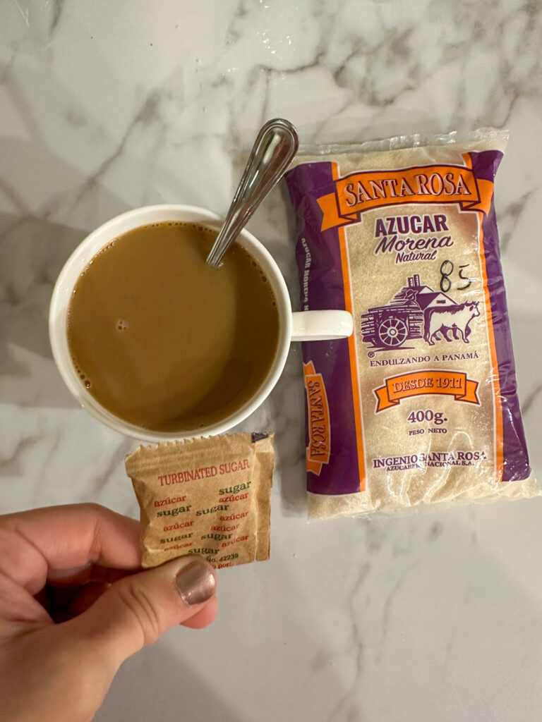 cafe con leche in white mug beside turbinated sugar packet and azucar morena in Panama City for what to expect on first time to Panama