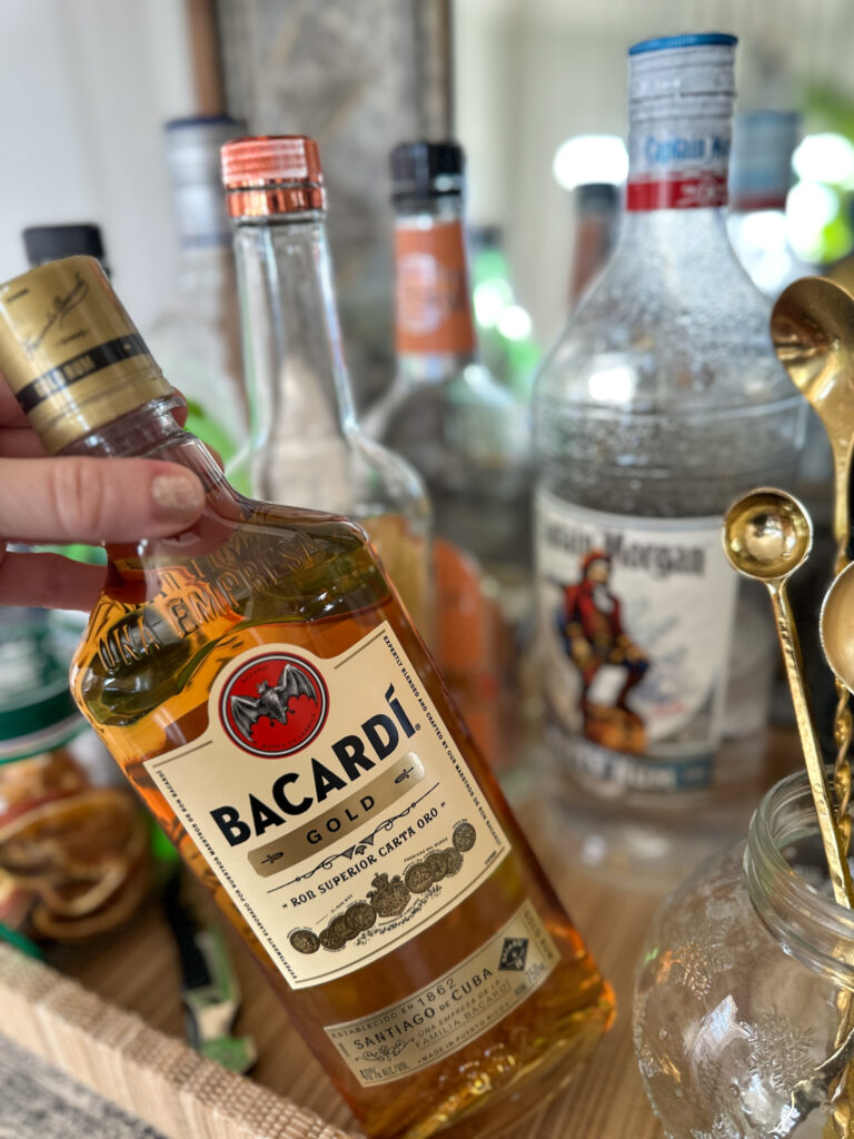 woman pulls Bacardi Gold from bar tray to go with her cocktail of the month planner