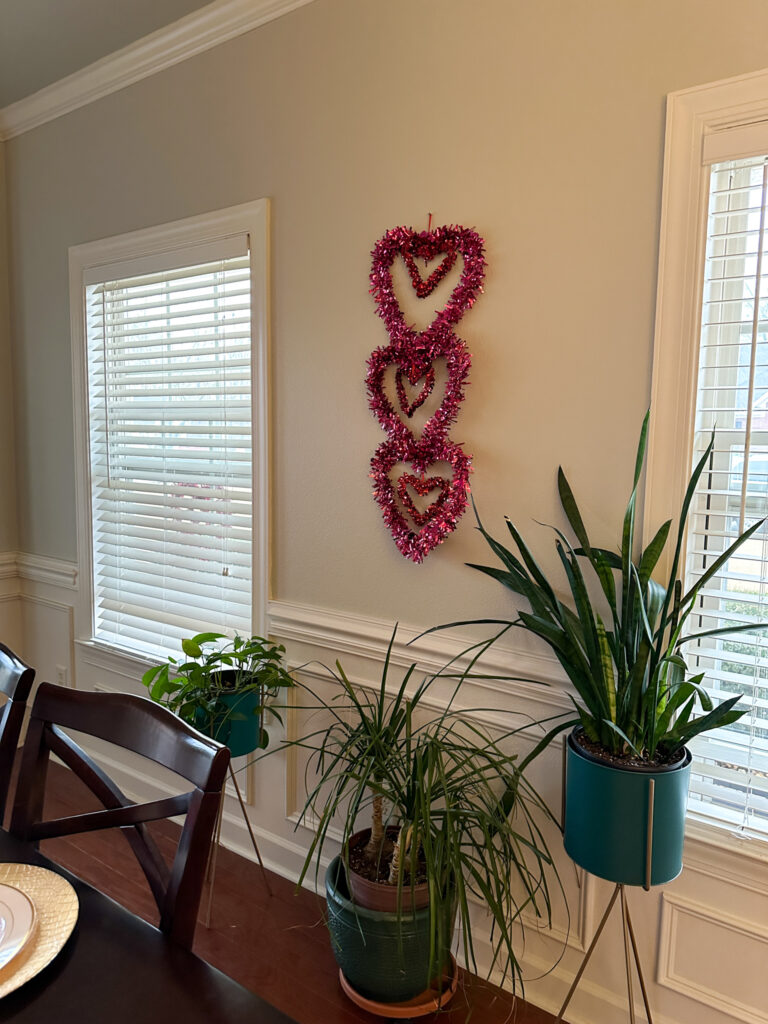 trio of tinsel hearts hanging on wall above plants