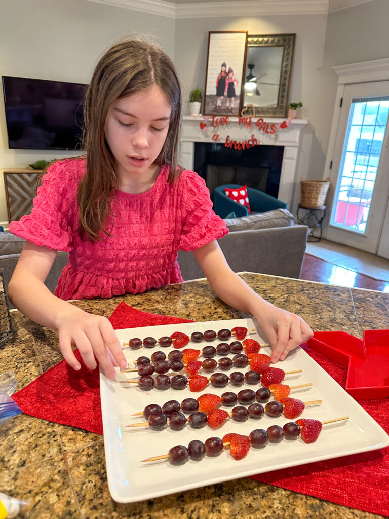 girl puts together fruit heart skewers for a mom-and-me Galentine's brunch