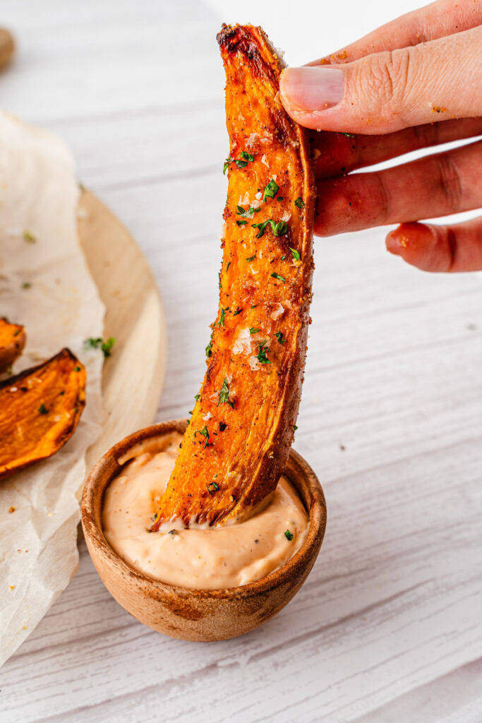 woman holds air fryer sweet potato wedge in dipping sauce