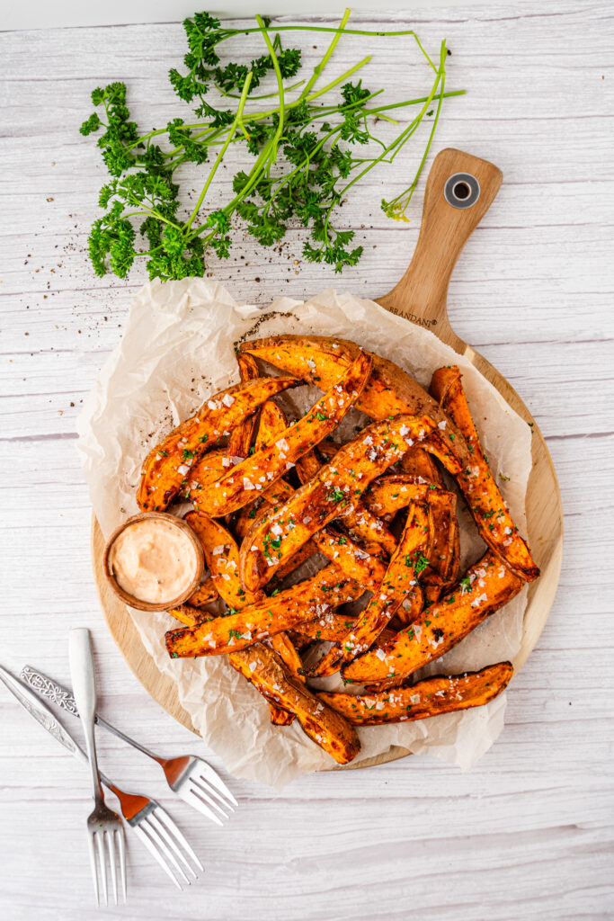 air fryer sweet potato wedges on a round serving platter with parchment paper and forks