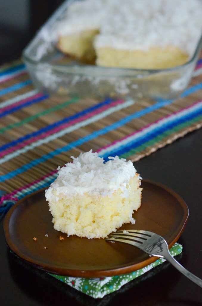 cream of coconut poke cake slice on wooden plate with fork