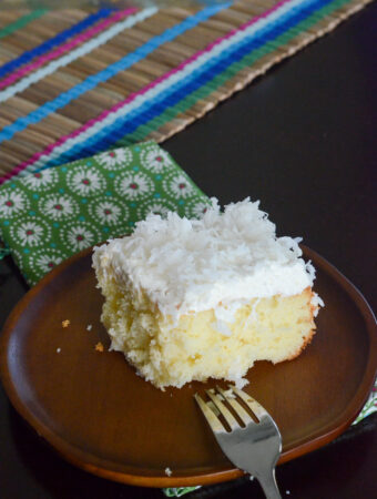 small piece of cream of coconut cake on bamboo plate with green napkin and fork