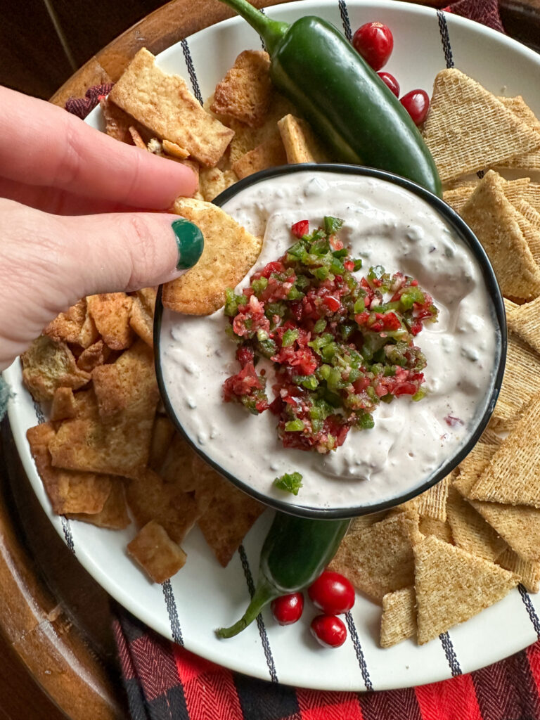 woman dips cracker into cranberry jalapeño dip in bowl surrounded by crackers