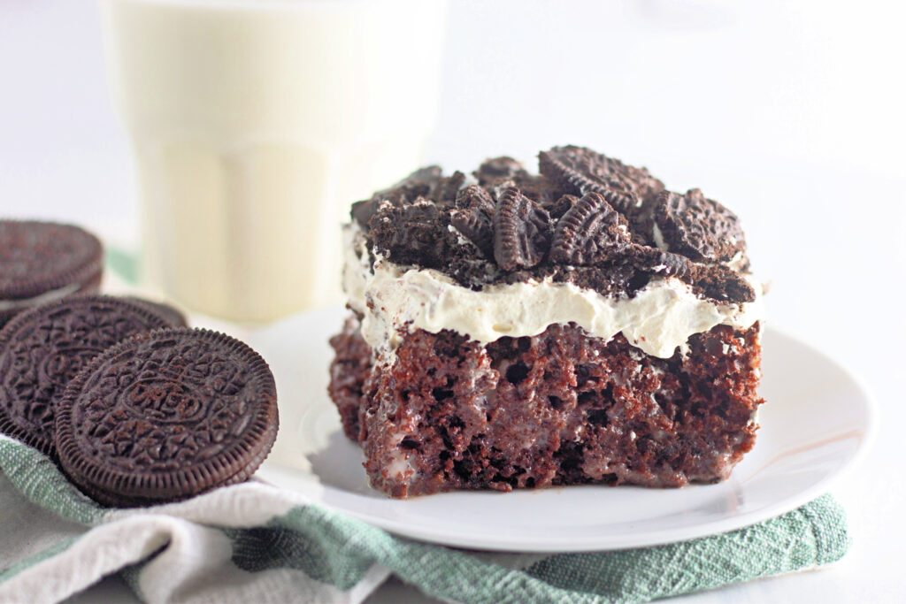 chocolate Oreo cookies and cream poke cake on white plate with Oreos to the left