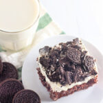 Oreo poke cake slice (cookies and cream cake) on a plate near milk and Oreos