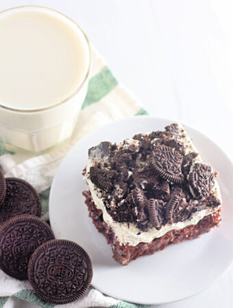 Oreo poke cake slice (cookies and cream cake) on a plate near milk and Oreos