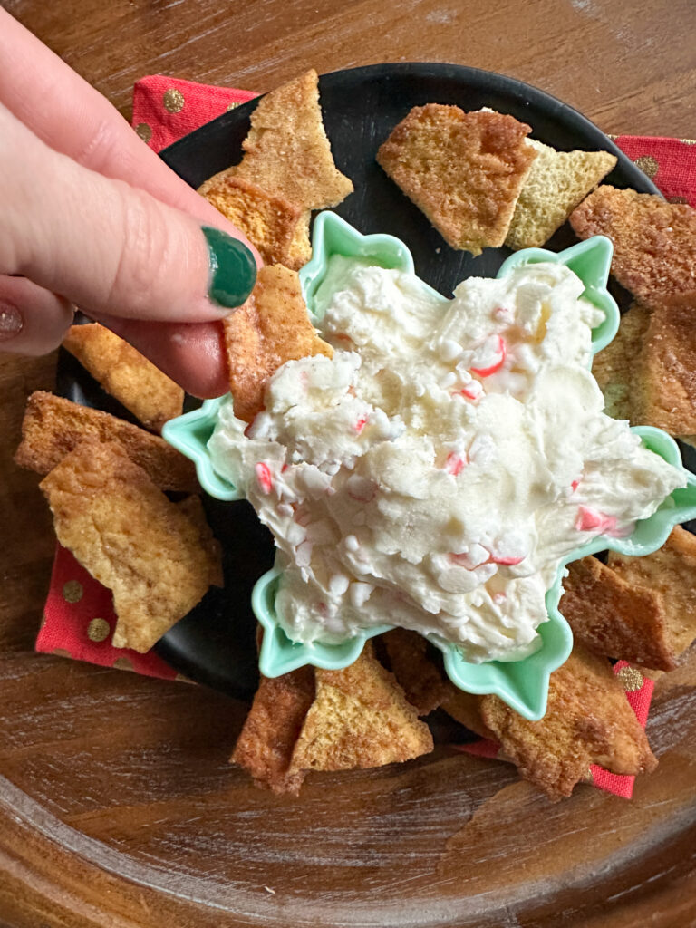 woman dips cracker into a festive peppermint dip in a winter bowl
