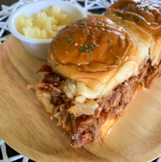 pulled pork pineapple sliders on plate with white cup of pineapple at back