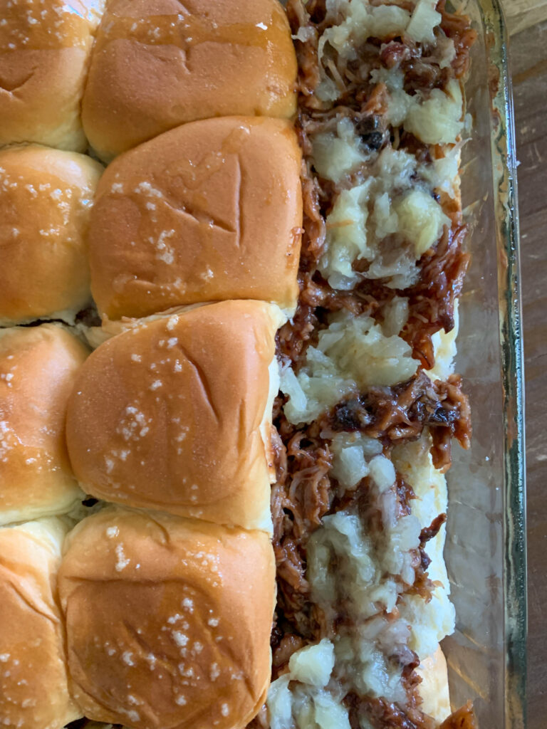 pulled pork and pineapple tidbits on slider rolls in glass pan, prepping for the oven