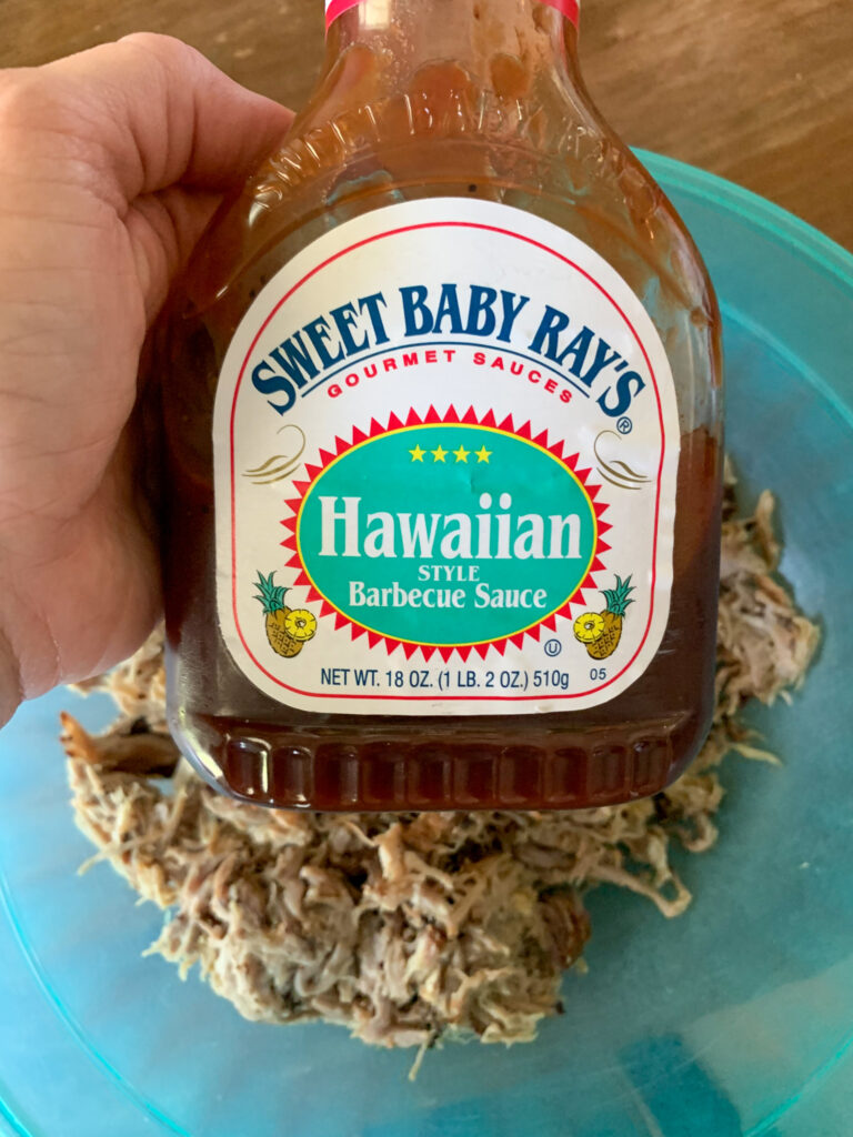 woman holds Sweet Baby Ray's Hawaiian Barbecue Sauce over bowl of pulled pork
