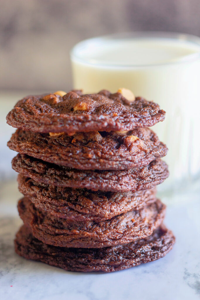 chocolate cookies with peanut butter chips stacked in front of glass of milk