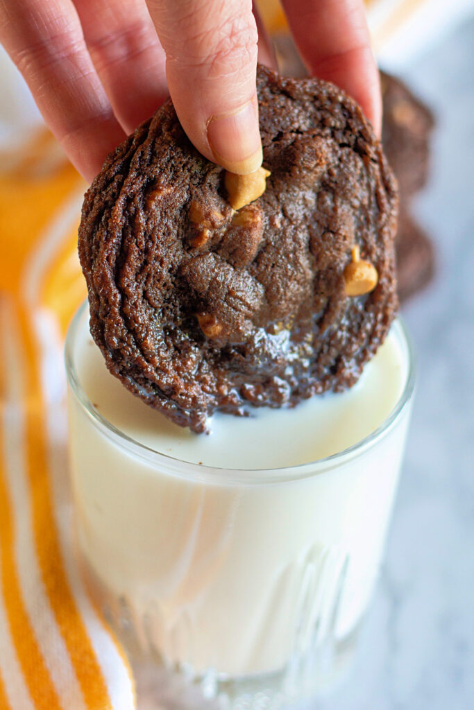 chocolate peanut butter chip cookie dunking into glass of milk