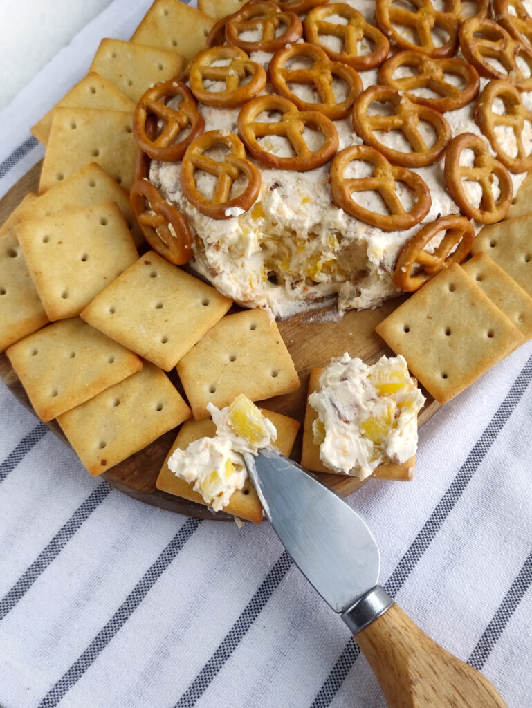 bacon cheddar pineapple cheese ball with crackers and a knife