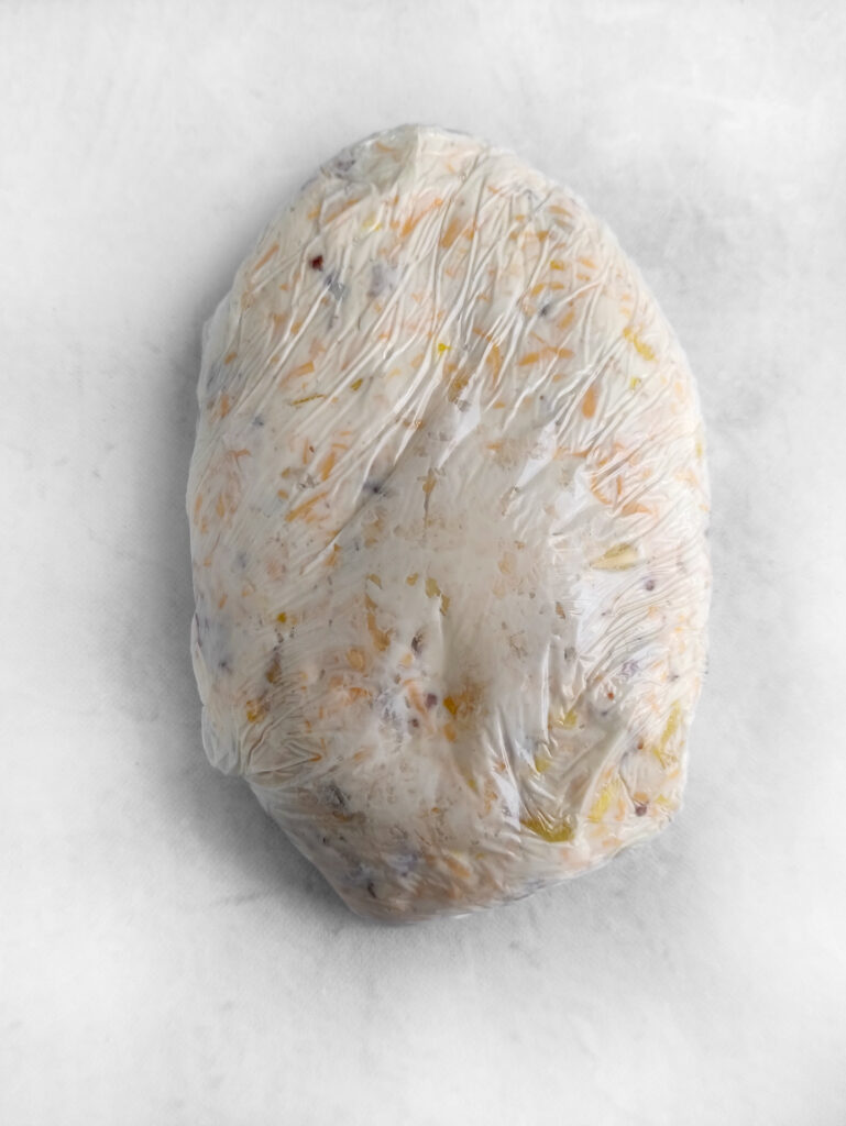 bacon cheddar pineapple cheese ball wrapped in plastic wrap