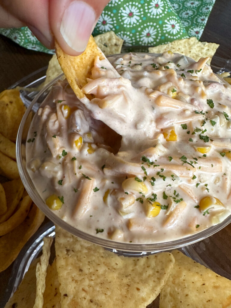 hand scoops cold Mexicorn dip with Rotel out of glass bowl