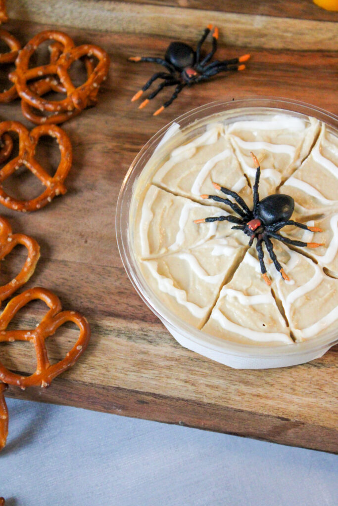 spiderweb Halloween hummus with a spider on top beside pretzels