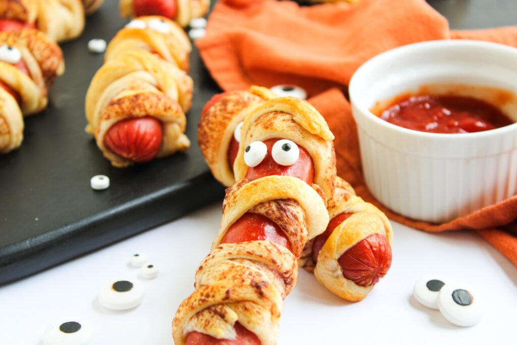 mummies in a blanket beside small dish of ketchup