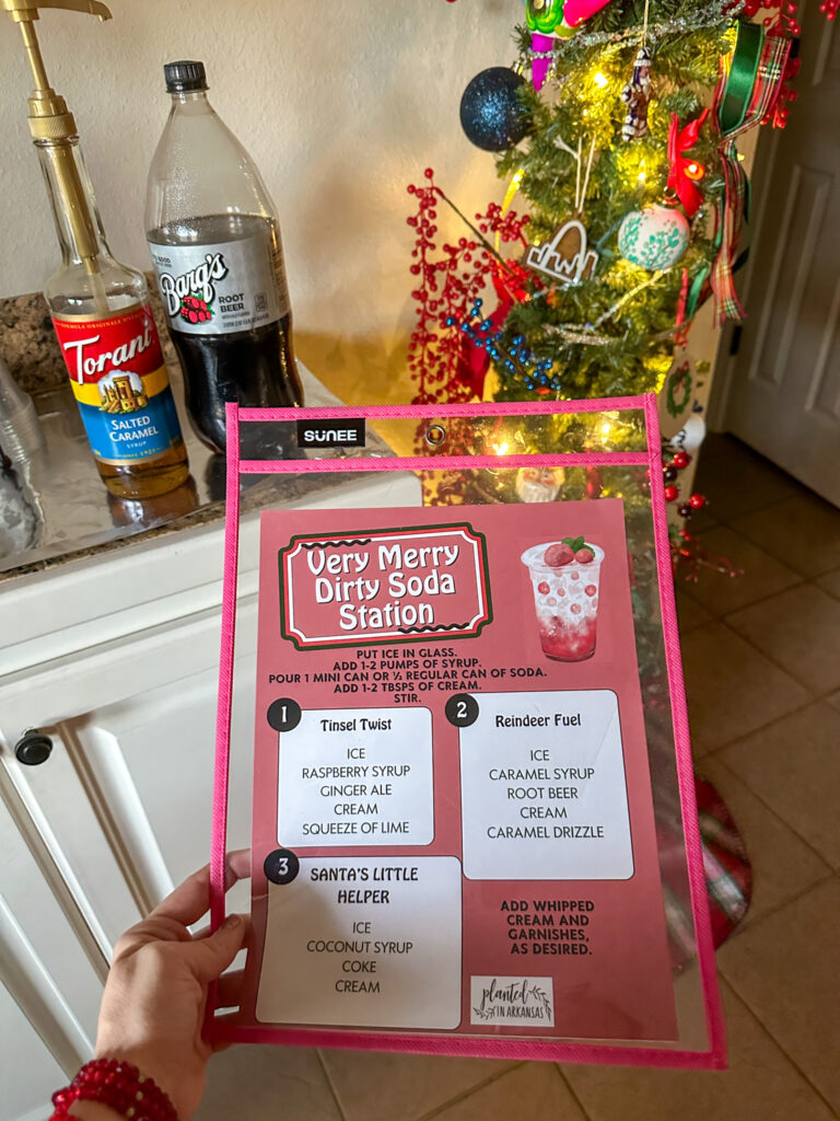 woman holds free printable Christmas dirty soda menu in front of small tree