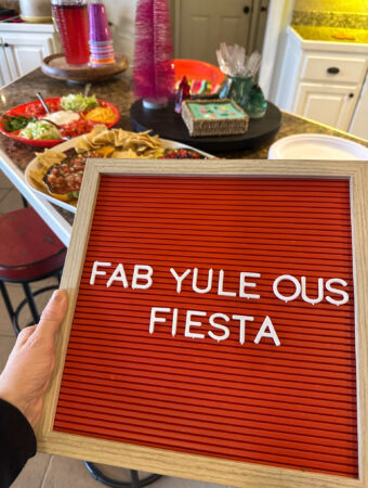 woman holds fab-yule-ous fiesta sign in front of Christmas dinner spread