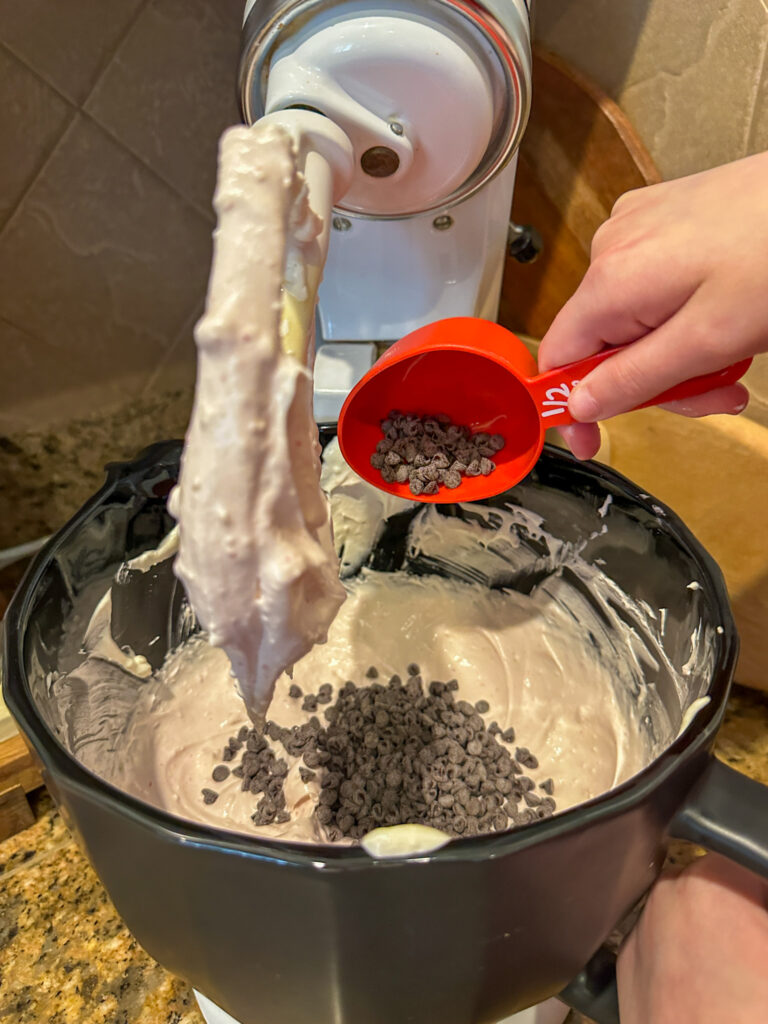 child pours mini chocolate chips into mint chocolate chip dip in mixing bowl