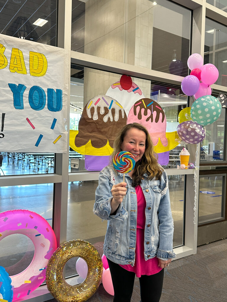 Arkansas blogger, Amy, stands with lollipop in front of decorations at teacher sweet send off party
